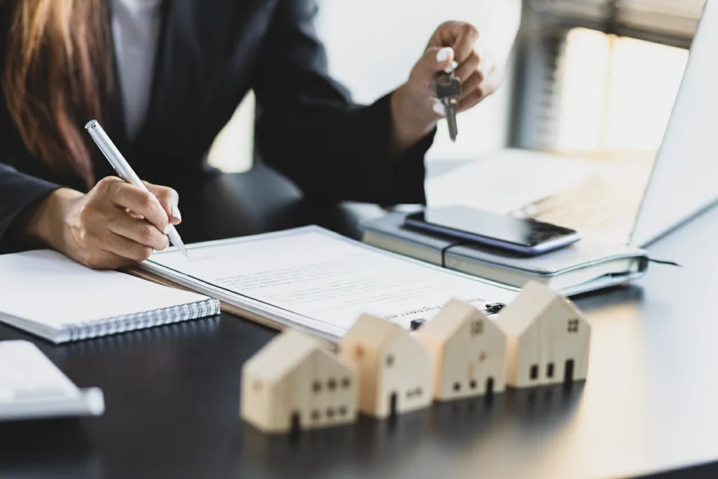 rentabilité locative : femme tenant un clé et un stylo devant un document et une maquette de maison