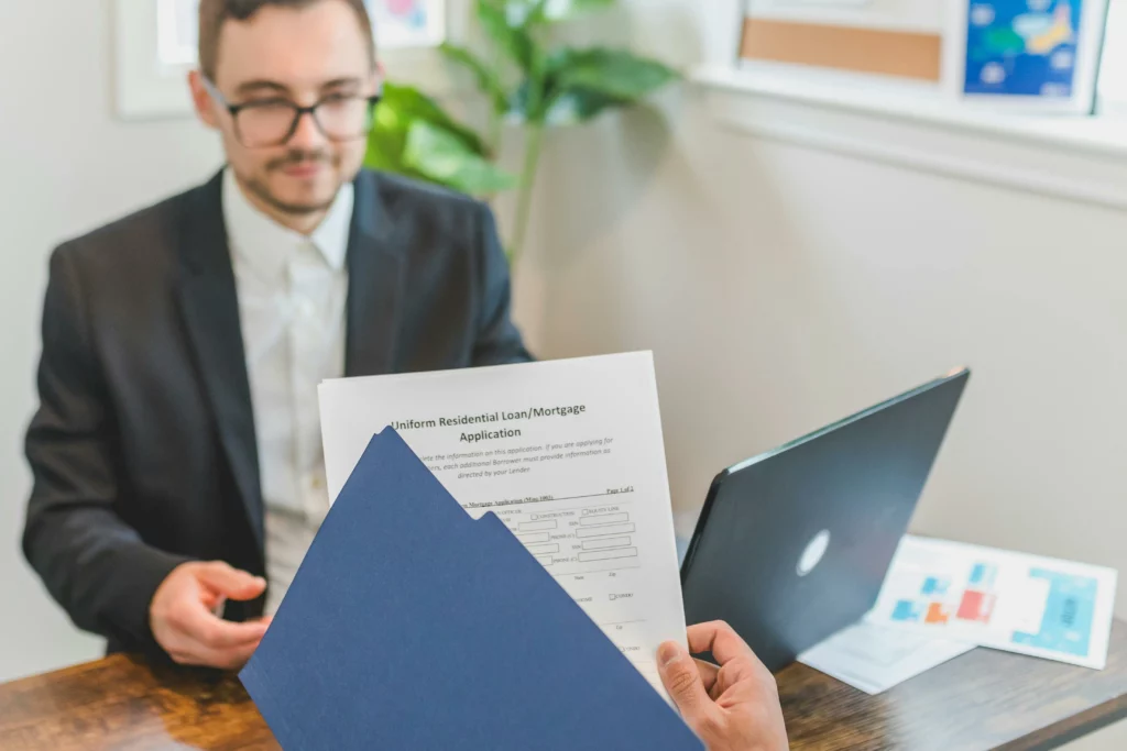 pret taux zero : homme devant un ordinateur portable et des mains tenant des documents