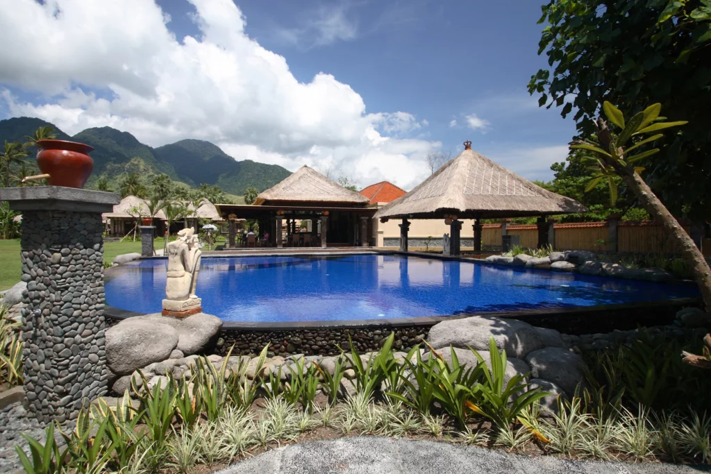 Un complexe de villas luxueuses à Bali avec une piscine à débordement entourée de paysages tropicaux, des toits en chaume et des montagnes en arrière-plan.