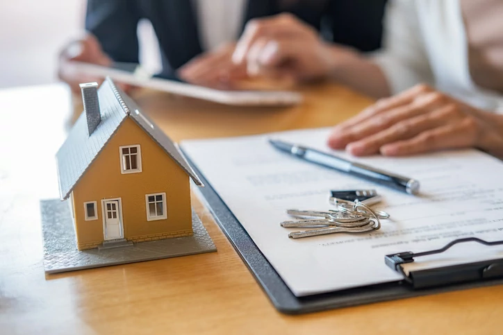 comment changer assurance prêt immobilier : deux personnes devant une petite maison, un document, une clé, un stylo et une tablette