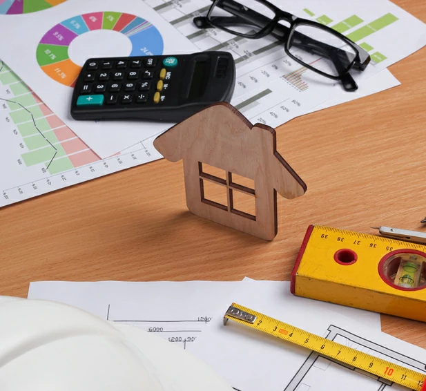 renovation thermique : plusieurs documents en papiers avec divers dessins et plan, des outils pour le bâtiment, une calculatrice, des lunettes et une petite maison en bois