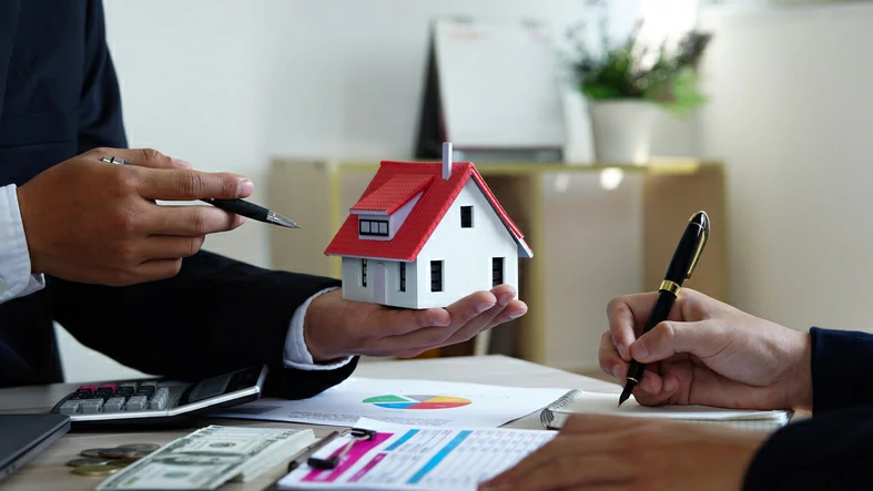 SIIC ou SCPI : main tenant une petite maison et un stylo devant une autre main qui écrit dans un bloc-note