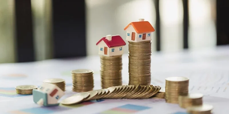 Des piles de pièces de monnaie, surmontées de petites maisons miniatures, symbolisant l'investissement immobilier et la croissance financière avec l'amortissement LMNP.